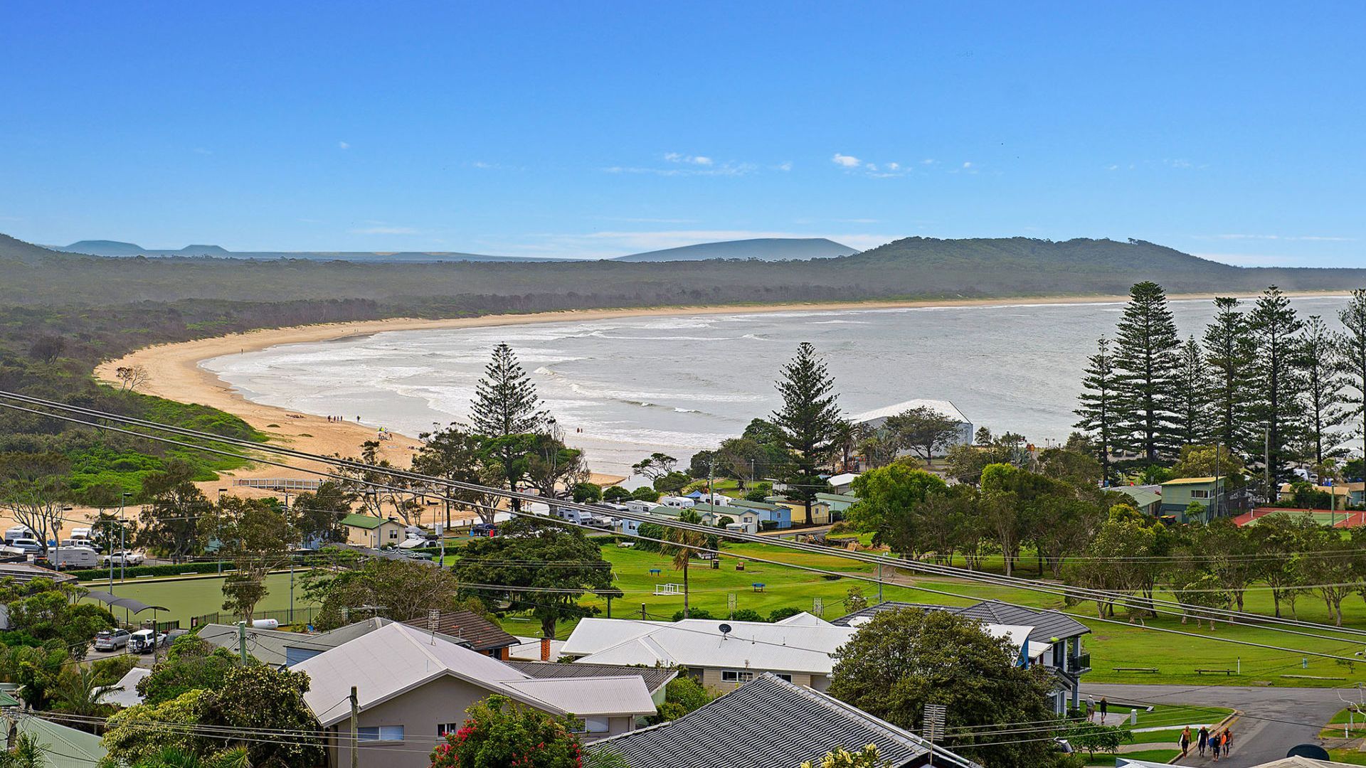 A coastal residential area with houses, a beach, and a clear sky.
