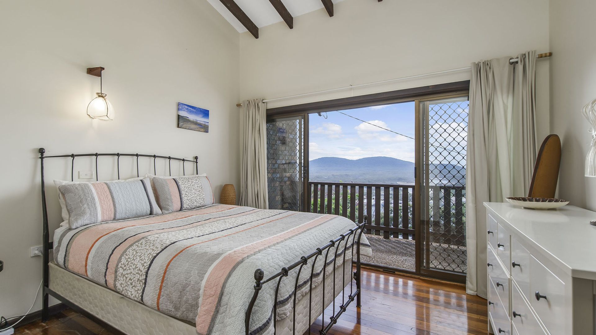 A bedroom with a bed, a nightstand, a dresser, and a view of the outdoors.