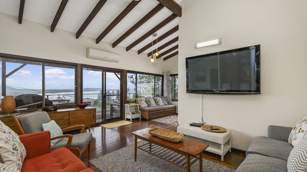 A spacious living room with a large TV, comfortable seating, and a view of the outdoors.