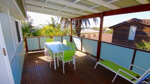 A covered outdoor area with a table and chairs, a wooden deck, and a view of a building and palm trees. - Good Vibes, 18 East Street (Crescent Head)