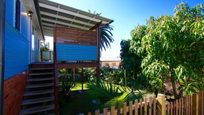 A two-story house with a wooden deck, a blue garage, and a garden with various plants.
