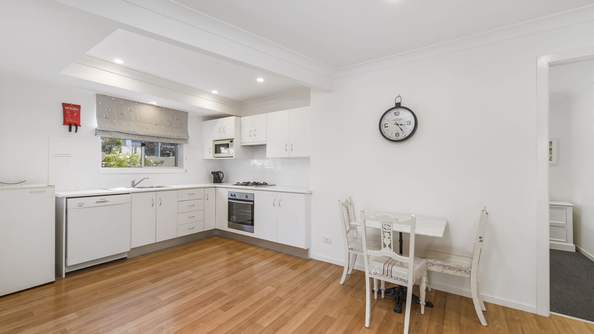A modern kitchen with white cabinetry, a microwave, stove, and a clock on the wall.
