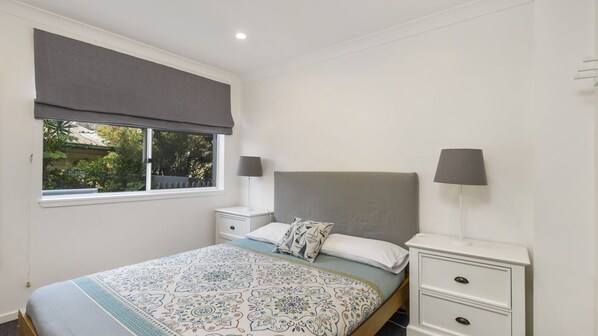 A bedroom with a bed, two bedside tables, a window with a view, and a nightstand with a lamp.