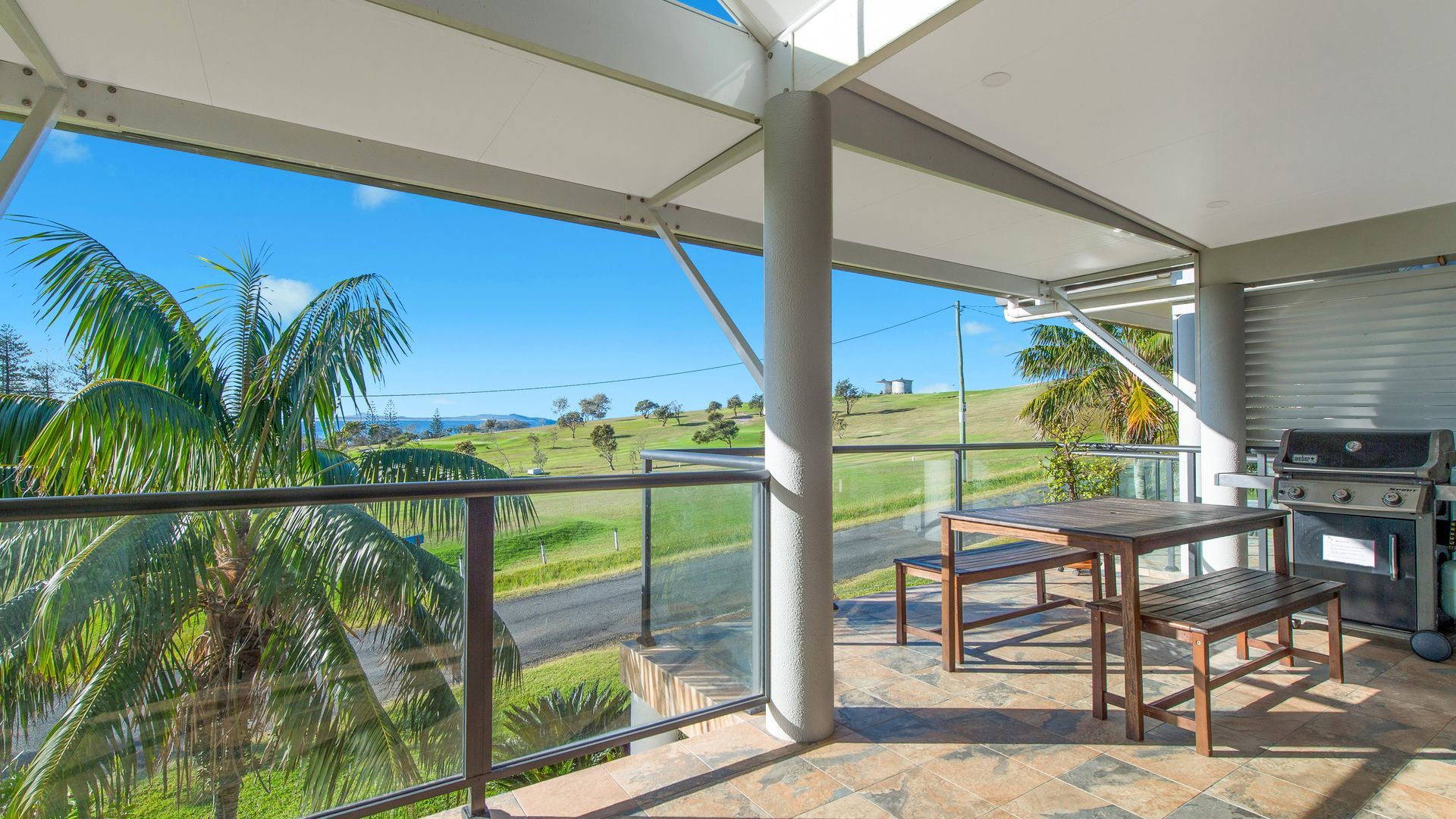 Un espacio exterior techado con una parrilla, una mesa y vistas a un paisaje verde.