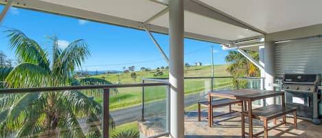 A covered outdoor area with a grill, a table, and a view of a green landscape.