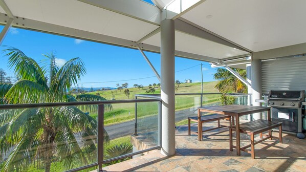 A covered outdoor area with a grill, a table, and a view of a green landscape. - Heathers Seaside Apartments 1, 10 Rankine Street (Crescent Head)