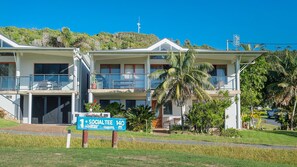 Un hotel de dos pisos con balcones, un cartel que indica medidas de distanciamiento social y abundante vegetación.