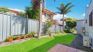 A residential property with a well-maintained lawn, a metal fence, and a variety of potted plants.