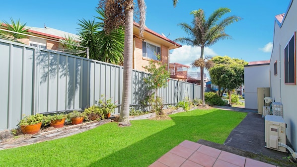 A residential property with a well-maintained lawn, a metal fence, and a variety of potted plants. - Heathers Seaside Apartments 2, 10 Rankine Street (Crescent Head)