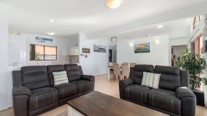 A modern living room with two black leather sofas, a wooden coffee table, and a dining area with a table and chairs. - Heathers Seaside Apartments 2, 10 Rankine Street (Crescent Head)