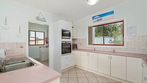A kitchen with a sink, oven, and a window with a view of greenery. - Heathers Seaside Apartments 2, 10 Rankine Street (Crescent Head)