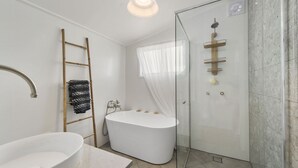 Een moderne badkamer met een vrijstaand bad, een douche met glazen wand en een houten trapje.