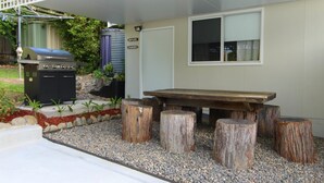 Een buitenterras met een barbecue, een houten tafel en een zithoek bestaande uit houten blokken.