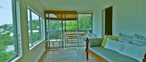 A balcony with a wooden table and chairs, a sofa with cushions, and a view of greenery.