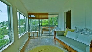 A balcony with a wooden table and chairs, a sofa with cushions, and a view of greenery.