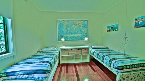 A room with two single beds, a world map on the wall, and a small shelf with baskets.