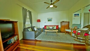 A living room with a flat-screen TV, grey sofa, wooden coffee table, wicker rocking chair, and a ceiling fan.