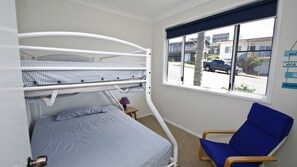 Una habitación con literas, una cama individual, una silla y un ventanal con vista a la calle.