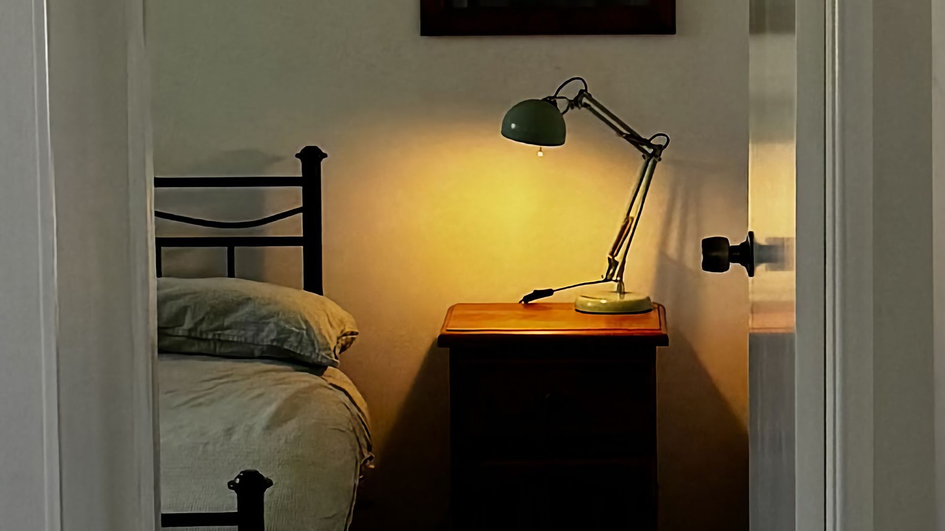 A bed with a headboard, a bedside table with a lamp, and a door frame.