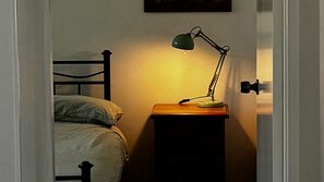 A bed with a headboard, a bedside table with a lamp, and a door frame.