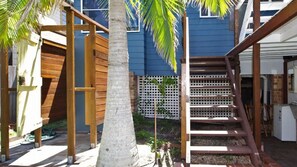A wooden deck with a palm tree, a white fence, and a staircase leading to a building with blue siding.