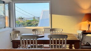 Un comedor con mesa y sillas, vistas al exterior y una lámpara al lado.