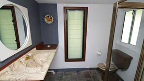 Un baño con lavamanos de mármol, un reloj montado en la pared, un ventanal con vidrio esmerilado y un inodoro con asiento marrón.