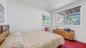 A bedroom with a bed, a dresser, a window with a view of greenery, and a wall-mounted mirror.