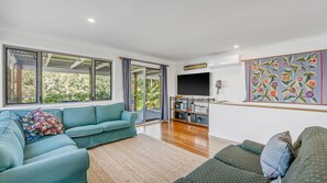 A living room with a teal sofa, a patterned rug, a bookshelf, and a flat-screen TV.