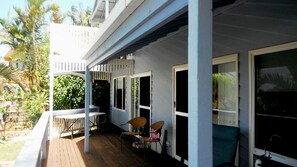 A covered outdoor area with a wooden deck, white railings, and a seating arrangement.