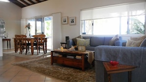 A living room with a sofa, a coffee table, and a dining area with chairs and a table. - Bellevue Holiday House Crescent Head (Crescent Head)