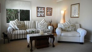 A living room with a striped sofa, a striped armchair, a wooden coffee table, and a lamp. There are framed pictures on the wall.