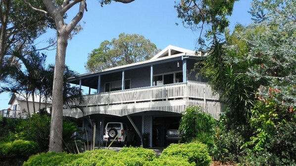 A two-story house with a balcony, surrounded by lush greenery.