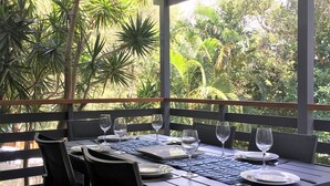 Un área de comedor al aire libre con mesas dispuestas para dos personas, rodeada por una barandilla de madera y con vistas a un exuberante jardín.