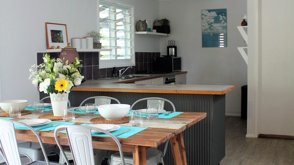 A modern kitchen with a dining area, featuring a wooden table, chairs, and a vase with flowers.
