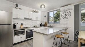 A modern kitchen with white cabinetry, stainless steel appliances, a large island with stools, and a wall clock.