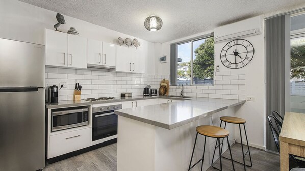 A modern kitchen with white cabinetry, stainless steel appliances, a large island with stools, and a wall clock.
