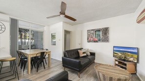 A modern living room with a dining area, a black leather sofa, a television, and a ceiling fan.