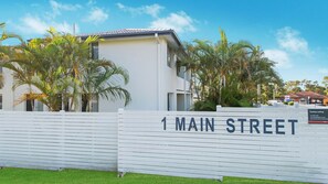 A residential property with a white fence, a sign reading '1 MAIN STREET,' and a building with a tiled roof.