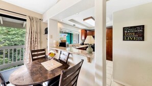 Un comedor con una mesa y sillas de madera, vistas a la cocina y un balcón con cortinas.