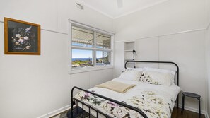 Een slaapkamer met een bed, een raam met uitzicht, een schilderij aan de muur en een bedlampje.