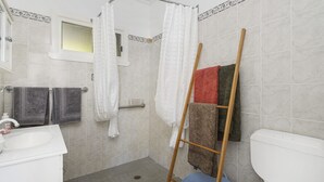 Une salle de bain avec une douche, des toilettes et un lavabo. Des serviettes sont suspendues sur un porte-serviettes et une échelle en bois est appuyée contre le mur.