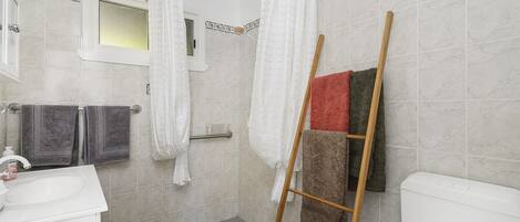 A bathroom with a shower, a toilet, and a sink. There are towels hanging on a rack and a wooden ladder leaning against the wall.