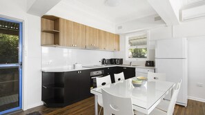 Een moderne keuken met een glazen tafel en stoelen, een zwart-wit kleurenschema en uitzicht op groen buiten.