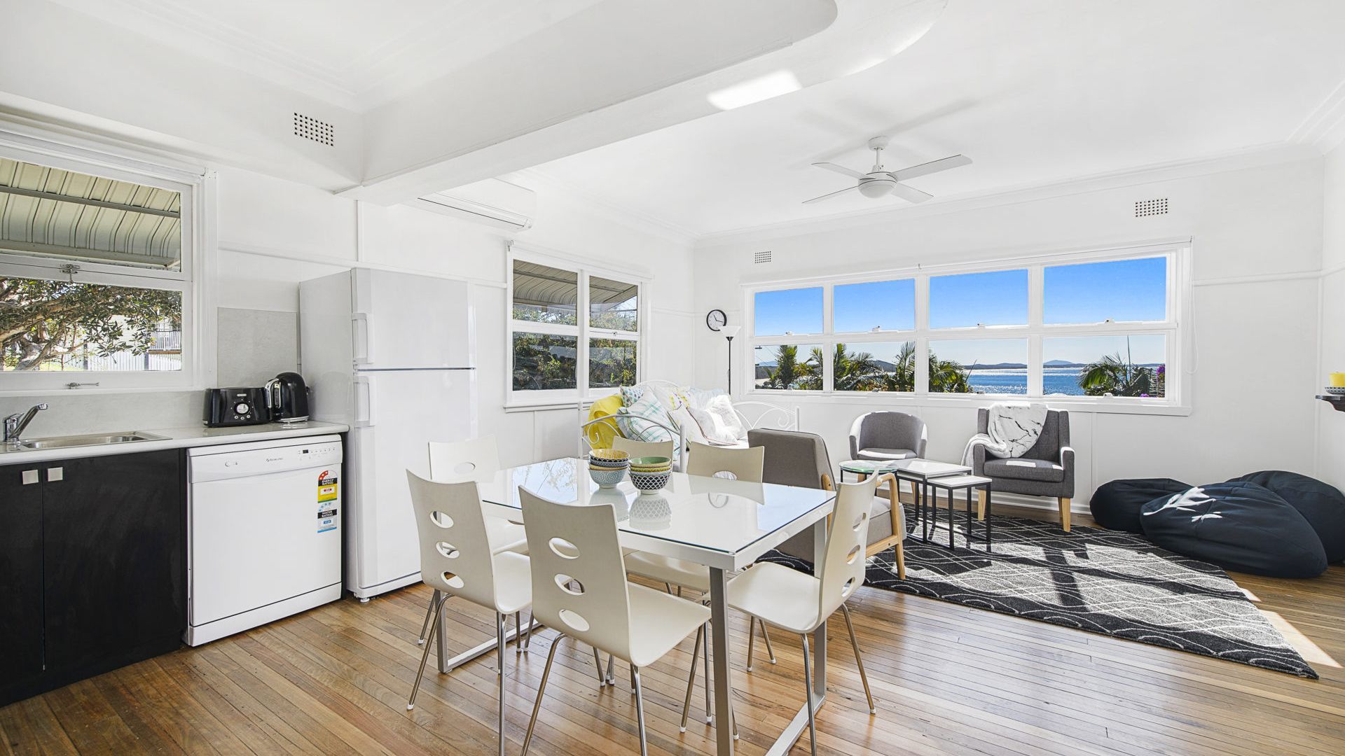 A modern kitchen with a dishwasher, a coffee maker, and a dining area with a table and chairs.