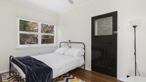 A bedroom with a bed, a window, a door, and a floor lamp.
