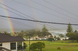 Área residencial com casas, um campo gramado e um arco-íris visível no céu.