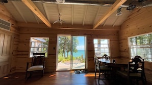 Una cabaña de madera con comedor, ventanas amplias y vista al océano.