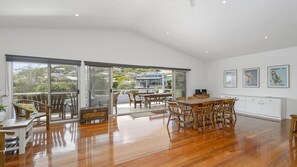 A spacious dining area with a wooden table and chairs, large sliding glass doors leading to a balcony, and a view of a residential area.
