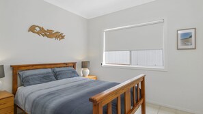 A bedroom with a bed, bedside tables, a window with blinds, a wall-mounted artwork, and a framed picture on the wall.